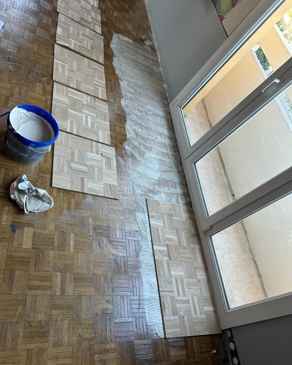 Parquet mosaïque à moitié vitrifié, le pot de vitrificateur posé au sol.