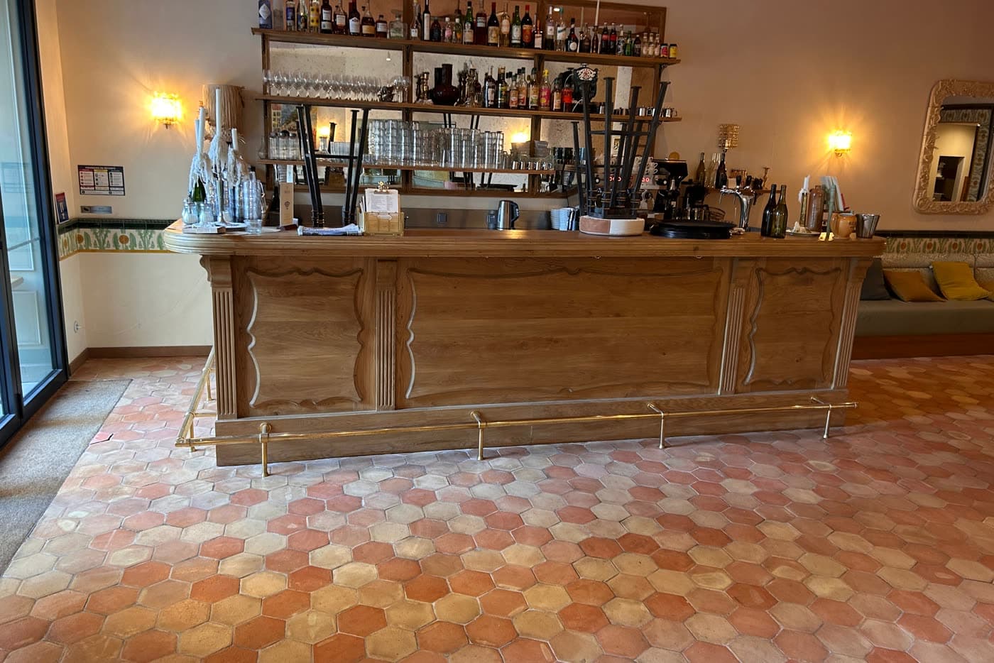 Salle d'un restaurant avec ses tomettes hexagonales rénovées, banquettes et comptoir en bois.