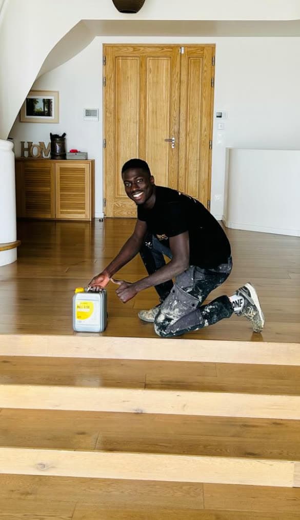 Tidiane Sylla, accroupi sur un parquet en chêne qu'il vient de finir, pouce levé.